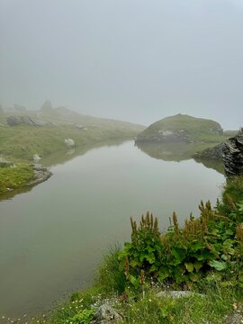 Vertical view of the peaceful B&acirc;lea Lake covered with soft mountain fog along the famous Transfăgărășan Highway in Romania, creating a serene alpine landscape