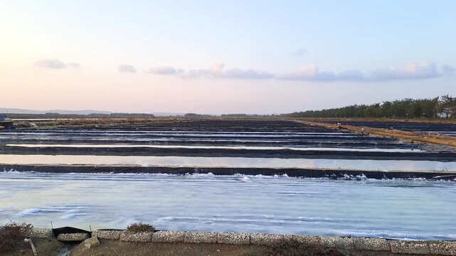 Wide aerial view of vast salt evaporation ponds in Sumenep, Madura, Indonesia. Traditional salt fields with water and salt crystals at sunset. Agriculture and industry landscape.