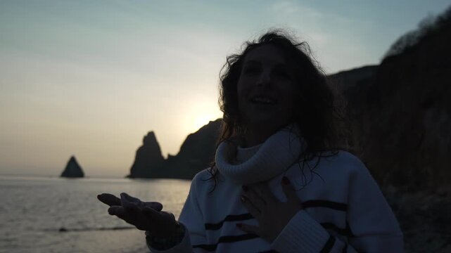 Woman singing and gesturing passionately near the sea stacks at sunset, expressing powerful emotion on the beach