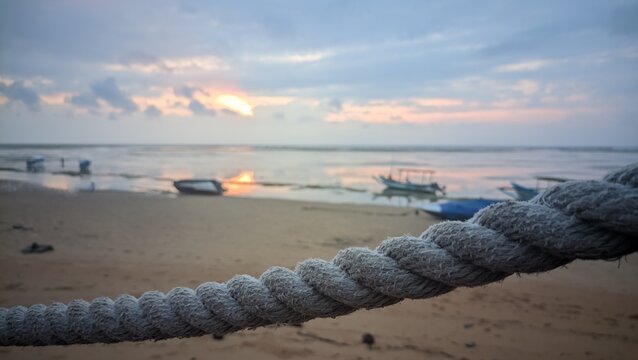 Close up of a thick weathered nautical rope with a blurred tropical beach sunset and traditional fishing boats in the background.