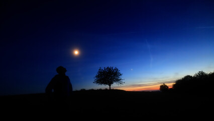 Silhouette of a person in nature observing night sky, Moon, stars and planets from a remote location. © astrosystem