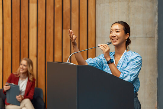 Woman speaking at a podium in a conference room with an audience and wooden wall