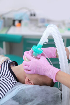 Close-up: doctor's hands in pink gloves fix an oxygen mask on face of small patient in pediatric clinic