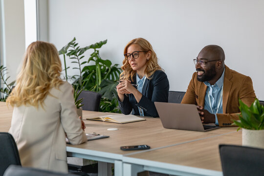 Business meeting with three professionals discussing ideas in a modern office setting with indoor plants