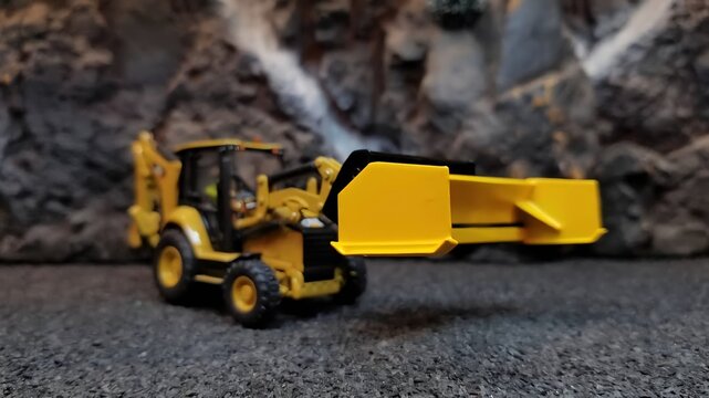 Yellow toy backhoe loader near rocky background