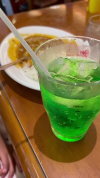 ファミレスでメロンソーダを飲む子供　