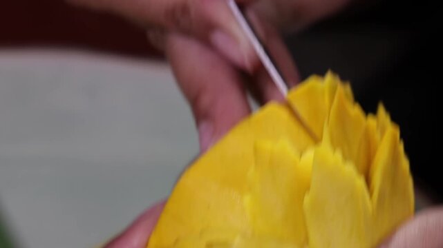 Close up human hand carving yellow fruit into intricate flower shape using small carving knife in Bangkok Thailand.