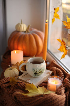 Aesthetic fall mood with coffee mug, open book, and glowing candles by the window