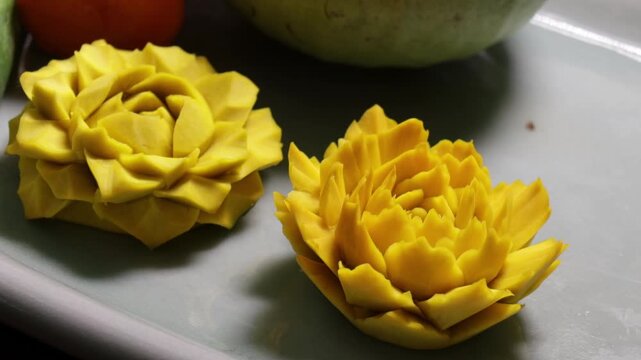 Close up human hand carving yellow fruit into intricate flower shape using small carving knife in Bangkok Thailand.