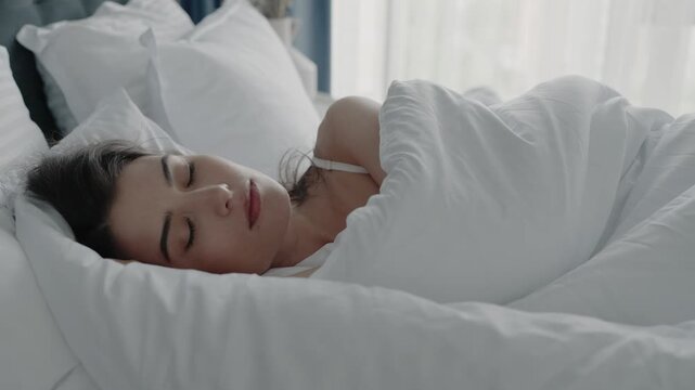 Portrait of a young woman sleeping calmly in a cozy bed with white sheets and pillows. The setting exudes comfort and tranquility, perfect for concepts of relaxation and rest.Woman Peacefully Sleeping