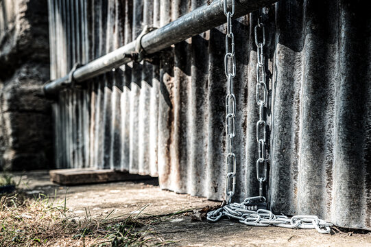 Surface level view of a long metal chain and combination lock attached to a metal pole on a building in the UK. Used to chain up bikes to prevent theft, common in this area.