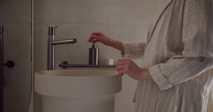 Close-up of person washing hands in a modern bathroom featuring a stylish, minimalist sink and soap dispenser. Person Washing Hands in Modern Bathroom with Stylish Sink and Minimalist Design