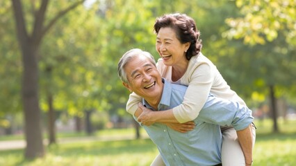 Fototapeta premium Happy senior Asian couple enjoying a playful piggyback ride together in a sunny green park during summer, showing joyful emotions and healthy lifestyle in nature with bright sunlight