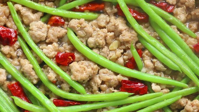 Stir-frying green beans with minced pork and dried chili in a hot pan. Top view shot
