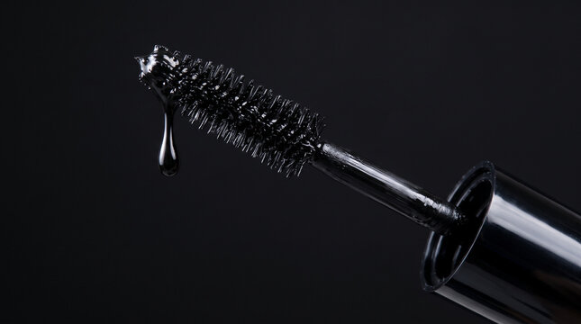 Mascara wand with dripping black formula on black background close up