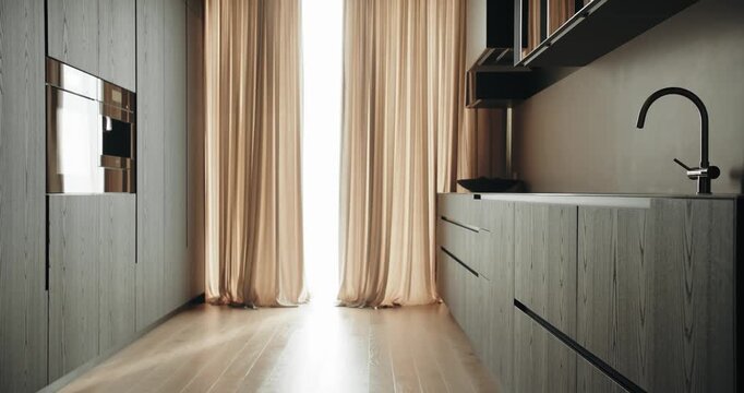 An elegantly designed modern kitchen featuring a seamless blend of wooden textures and minimalist style, highlighted by soft natural lighting from large windows draped with warm beige curtains.