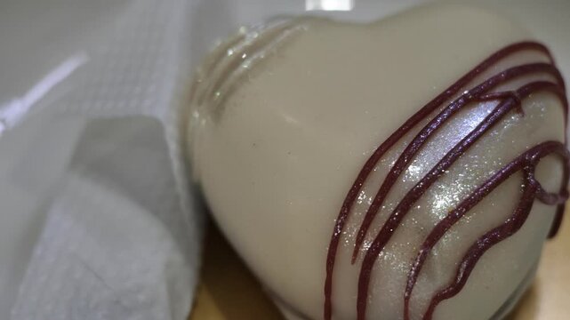 Extreme macro close-up slow motion shot showing shiny glitter glaze and dark chocolate drizzle details on a heart-shaped white mousse cake.
