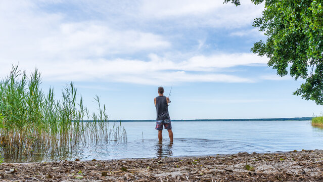 Ein junger Mann beim Angeln im Sommer an einem sch&ouml;nen See