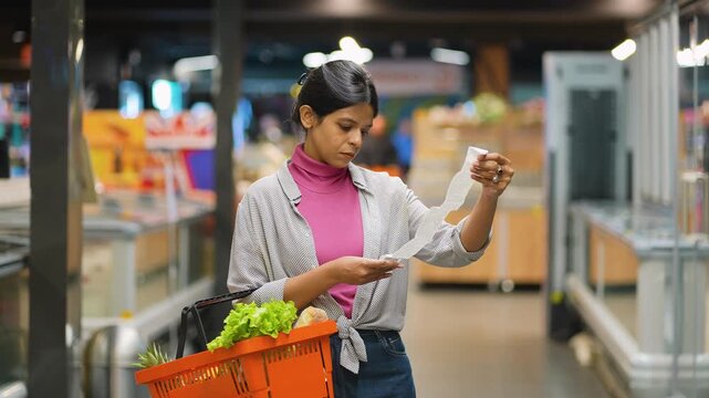 Frustrated Indian woman checking long grocery receipt in supermarket