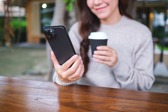 Closeup image of a woman holding and using smart phone while drinking coffee in cafe