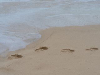 Soft waves kiss the golden sand. Footprints lead toward the sea's edge. Each step fades with gentle tide. Quiet calm lingers after the splash. Perfect for travel, nature, or relaxation themes © Freddy Chandra