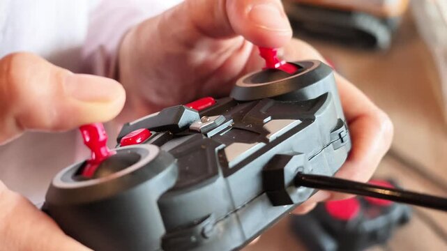 Macro slow motion video capturing thumbs pushing red joysticks on a black radio-control unit during vehicle operation.
