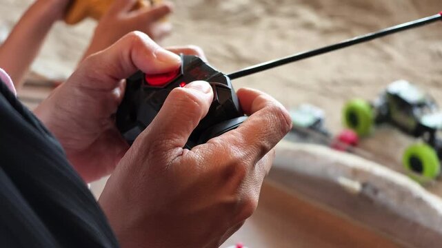 Slow motion close shot of hands actively moving joysticks on a black radio-controlled toy transmitter during play.
