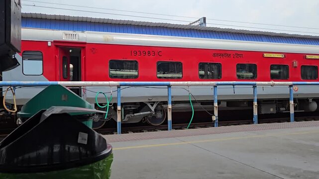 A stationary bin frames the rush of another red LHB train arriving on the platform. The rhythmic motion brings dynamic energy, highlighting station life, daily commutes, and swift Indian transit.