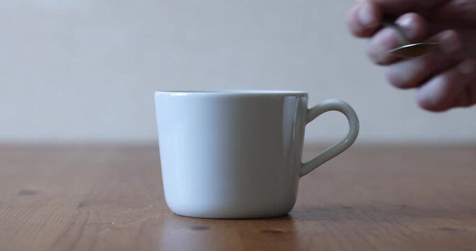 Pouring Sugar from Stainless Steel Teaspoon into Cup Side View