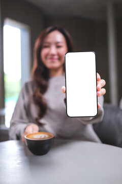 Vertical mockup image of a woman holding and showing a mobile phone with blank white screen in cafe