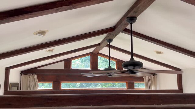 Ceiling fans spinning under vaulted ceiling with rustic windows