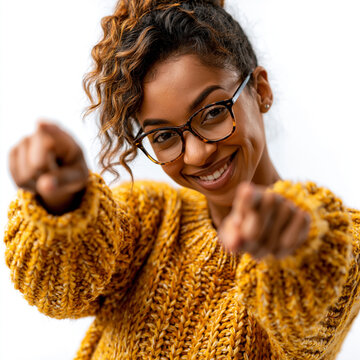 Smiling young woman wearing glasses and a yellow sweater pointing at camera with pointing