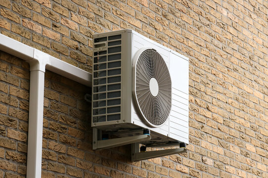 Airconditioning unit installed on brick wall. Summer heat wave prefention electronic cooling and ventilation appliance.