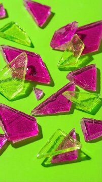 Shards of translucent pink and lime green candy are scattered across a bright green surface. The composition is vibrant and geometric with sharp shadows. Ideal for food or abstract backgrounds.