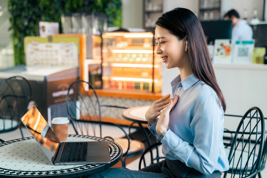 smiling Asian businesswoman having online video call on laptop with wireless earphones