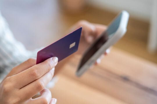 Woman holding a purple credit card in one hand and a smartphone in the other, making a secure mobile payment and engaging in online shopping or e-commerce from home