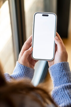 Person holding a modern smartphone with both hands, showing a blank white screen ready for custom content and creative advertising, symbolizing communication, technology, and connectivity