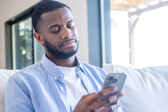 Young man sitting indoors, intently reading content on his smartphone with a skeptical and disbelieving expression, reflecting on digital information