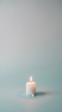 A small white candle with a ribbon burning brightly against a serene light blue background.