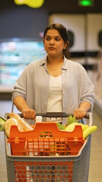 Indian woman pushing shopping cart in supermarket grocery aisle