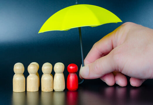 Hand placing a leader figure under umbrella representing motivation, support, and protective leadership.