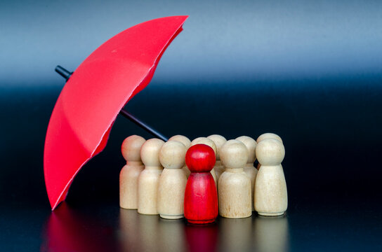 Red umbrella protecting wooden figures representing insurance coverage, risk management, and strong leadership support.