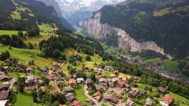Wengen Swiss village drone vertical dive down steep cliffs into Lauterbrunnen Valley Alps. Scenic top-down camera movement over traditional chalets, massive rock walls, waterfalls, mountains 4K.
