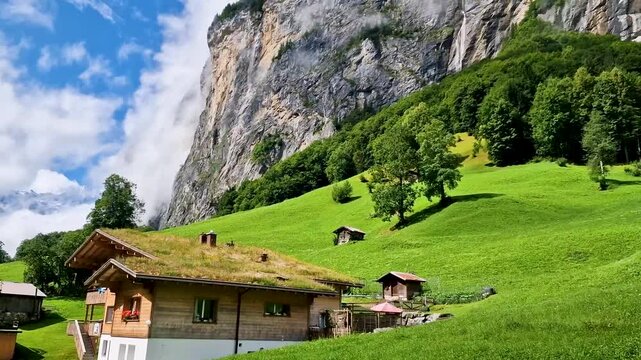 Lauterbrunnen village in Swiss Alps with scenic waterfalls and wooden chalets in green valley on sunny morning. Panoramic view of idyllic alpine landscape with clouds on cliffs in 4K travel footage
