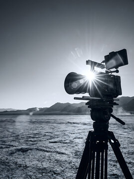 C&aacute;mara de cine profesional en tr&iacute;pode rodando en el desierto con destello de sol en blanco y negro