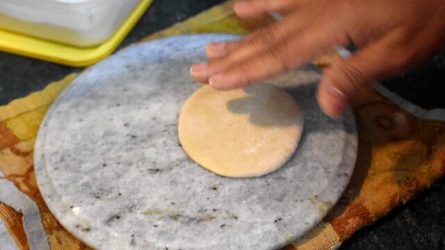 hand gently patting and shaping wheat dough on a traditional chakla before rolling it into roti