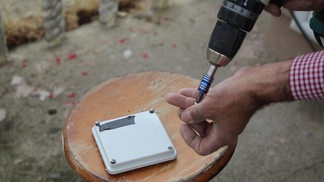 Professional electrician fastens screws into a junction box with a cordless drill before mounting a CCTV security camera.