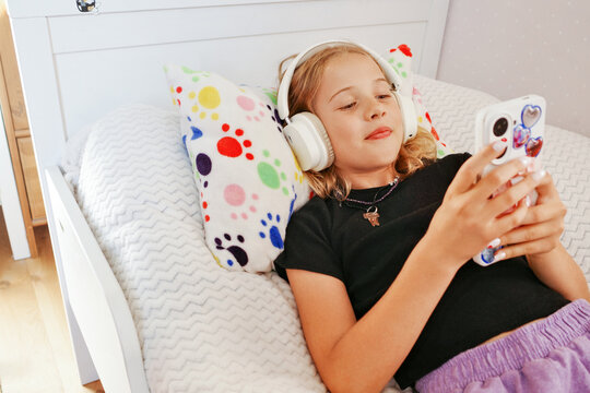 Teen relaxing in bed with headphones and smartphone