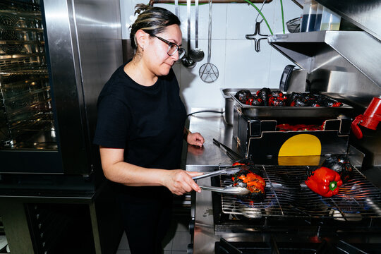 Chef roasting bell peppers on kitchen grill over flame