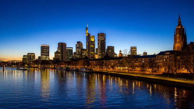 Frankfurt, Germany, a view of the illuminated financial district from the Main river with sightseeing boats at blue hour and cloudless sky  in the evening